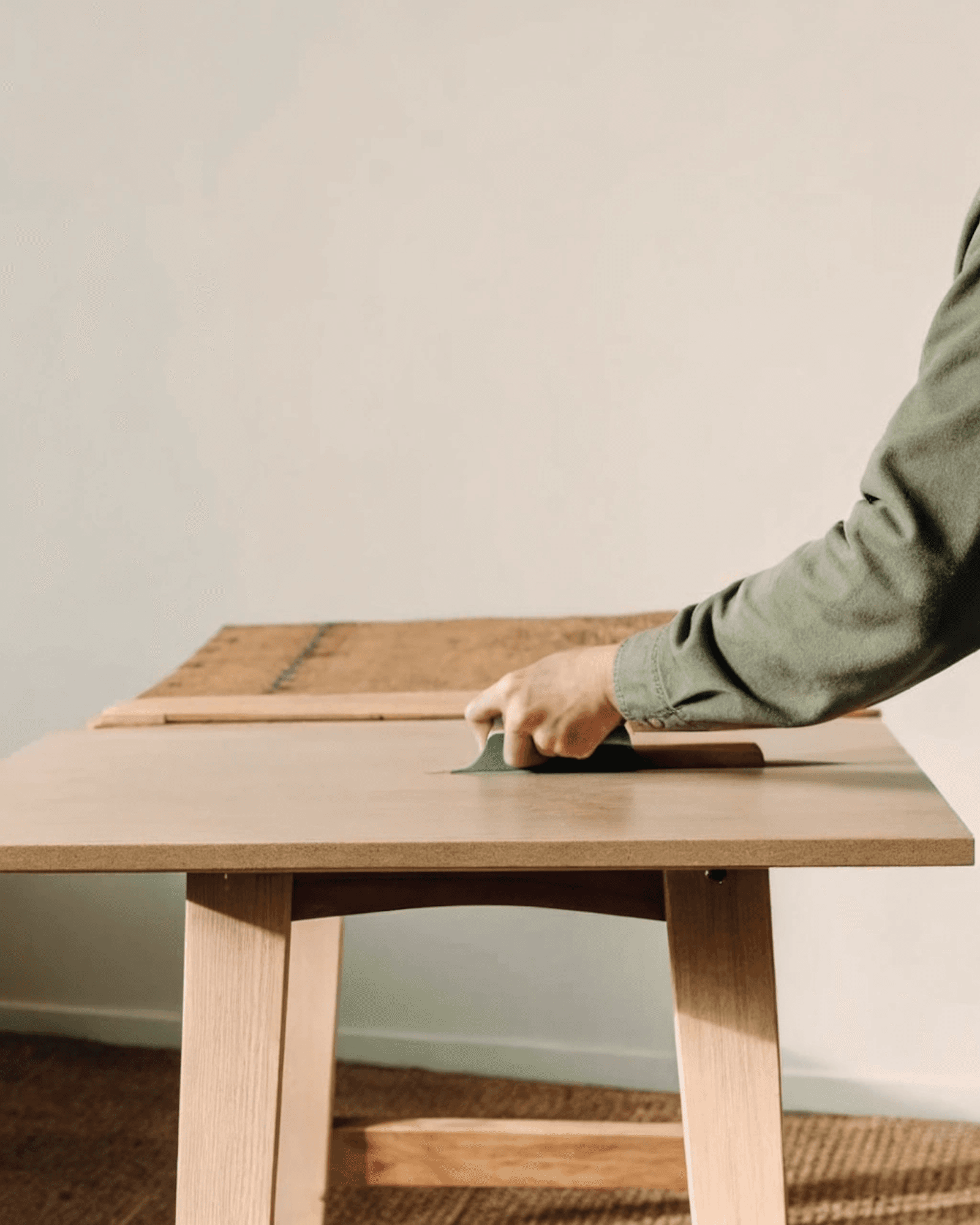 Hands sanding a light wooden tabletop in a bright room